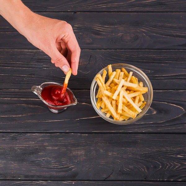A bowl of fresh golden french fries with a dipping sauce of ketchup on the side.