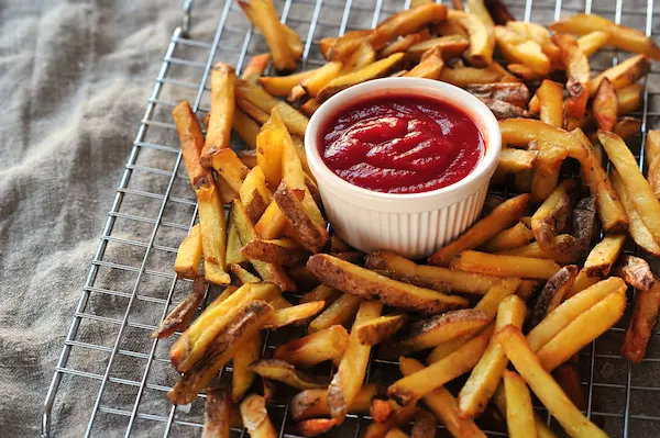 A bundle of freshly fried fries on a cooling rack with a small white bowl of dipping sauce placed in the center.