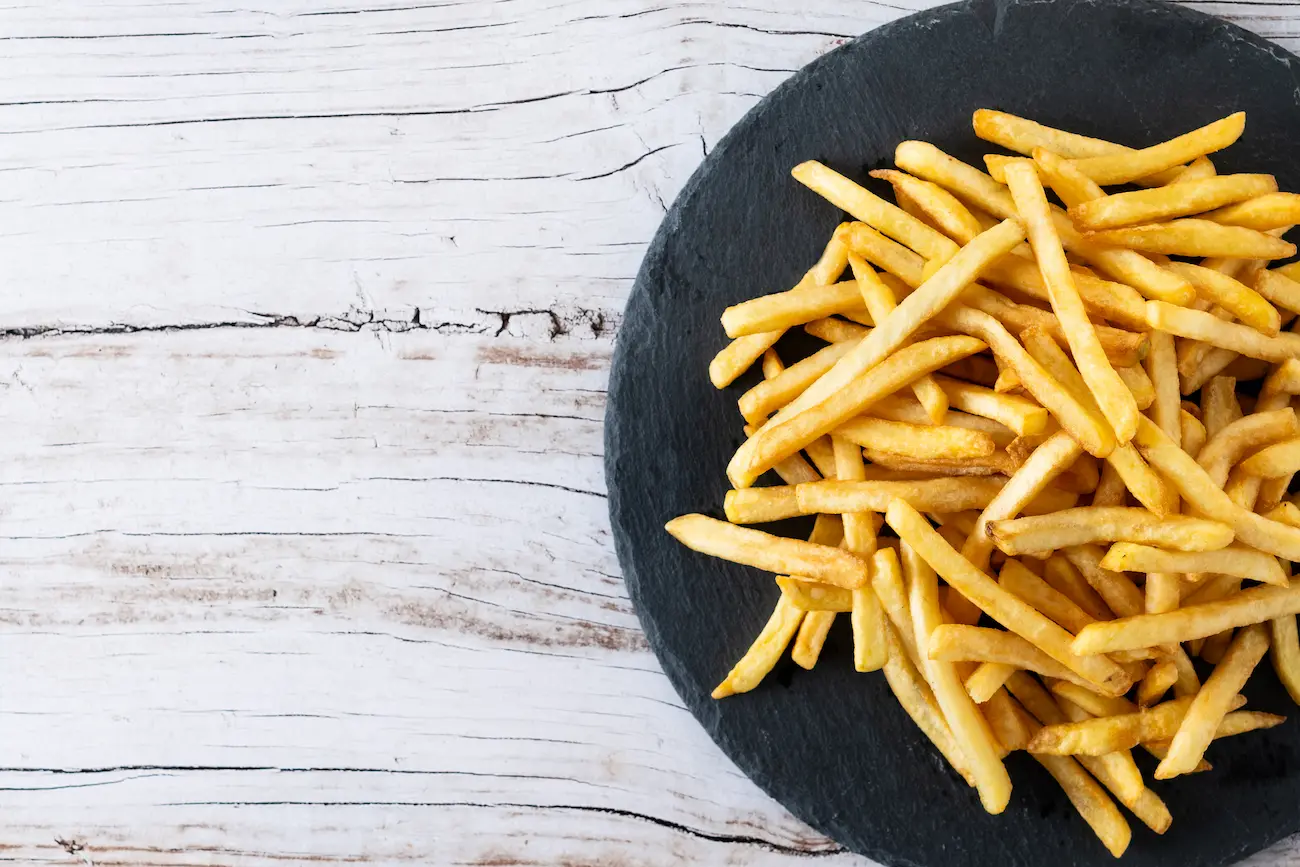 A grey stone plate topped with yellow french fries on a white wooden table.