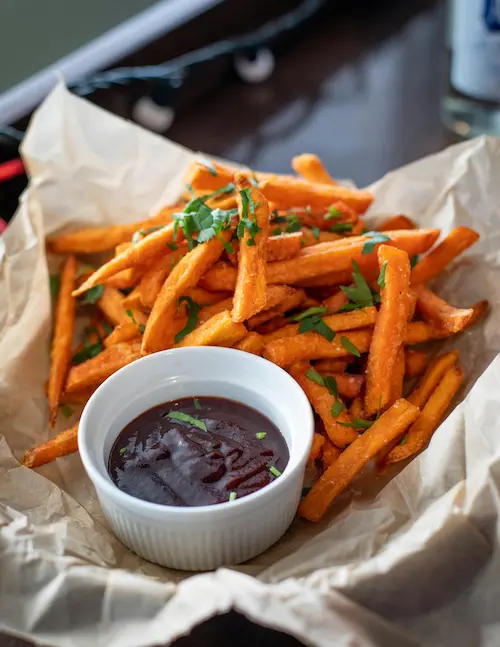 A bowl of french fries garnished with green parsly, accompanied by a small bowl of gravy dip.